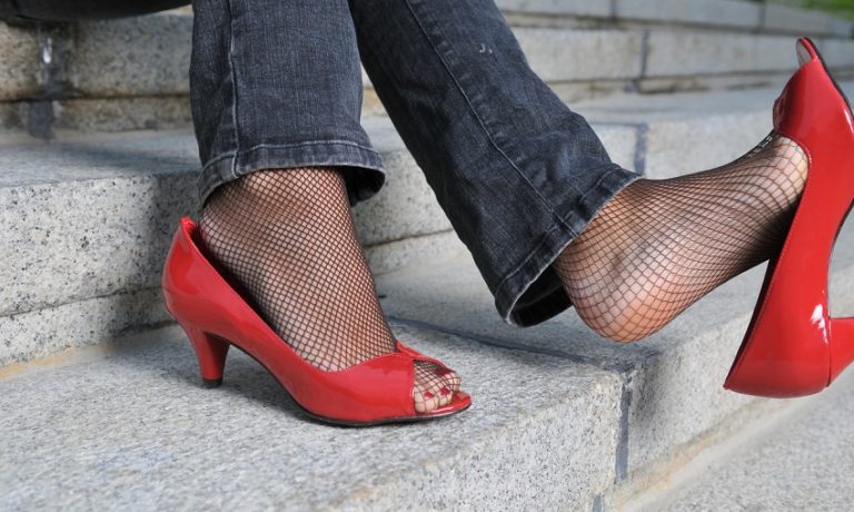 Füße einer Frau mit Netzstrümpfen und roten High Heels