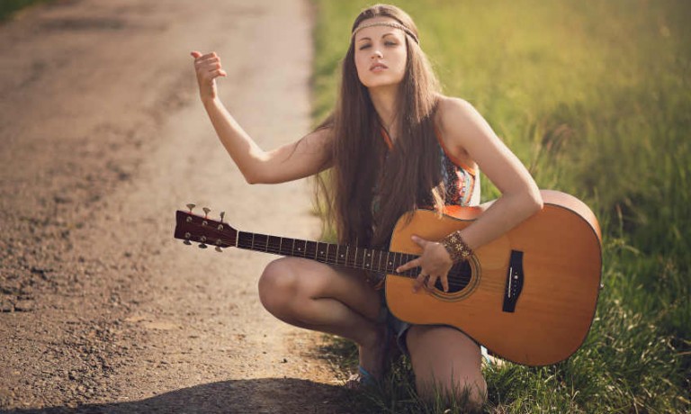 Hippie Hipster Mädchen wartet als Anhalterin mit einer Gitarre an einer Straße