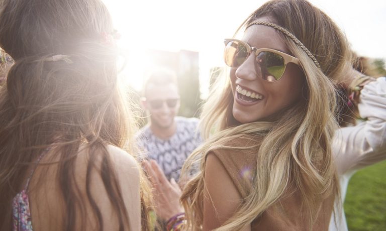 Blondes Mädchen mit Sonnenbrille tanzt mit ihren Freunden auf einem Musik-Festival