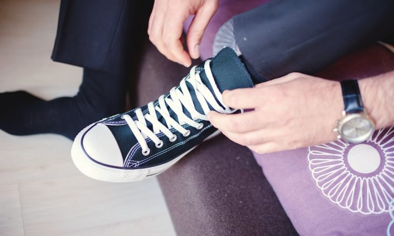Mann im Anzug bindet sich im Sitzen die Schnürsenkel seines linken Sneakers zu