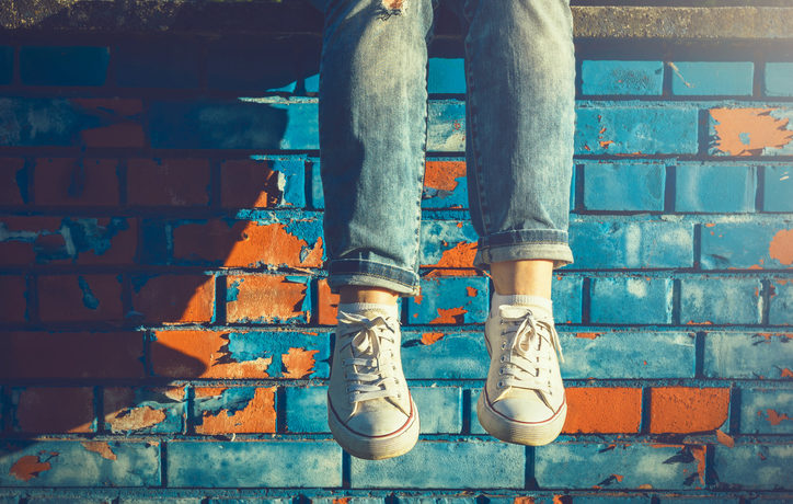 Beine einer Frau mit hochgekrempelter Jeans bis zum Knöchel vor einer Mauer